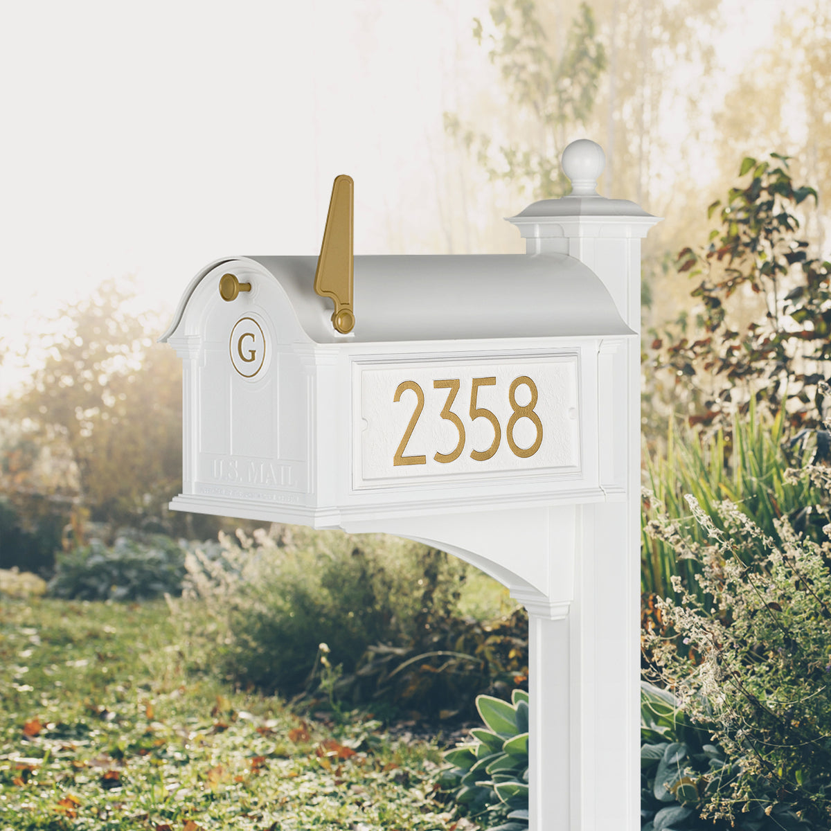 Modern Balmoral Monogram Mailbox & Post Package in white and gold, shown beside a lawn with sample address numbers and monogram